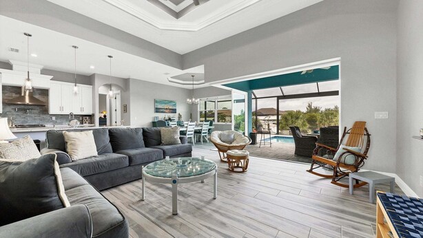 A modern living room with a grey sofa, a glass coffee table, wicker chairs, and a view of a pool and outdoor area. - Mpc15528 (Port Charlotte)