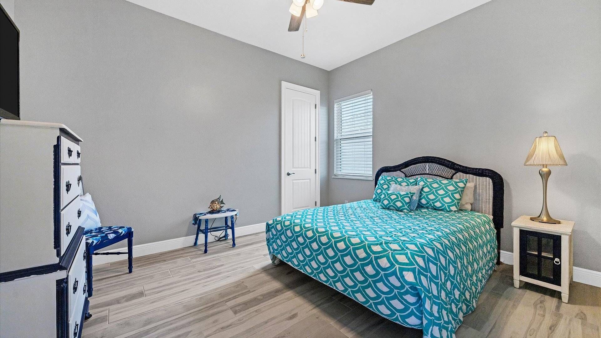 A bedroom with a bed, a nightstand, a chair, a dresser, a door, and a window with blinds.