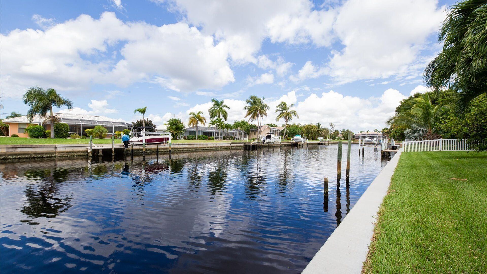 A canal with boats docked, surrounded by palm trees and houses.