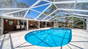 A covered outdoor swimming pool with a geometric roof structure, surrounded by a patio area with seating and a brick wall. - Lighthouse Retreat With A Pool (Ponce Inlet)