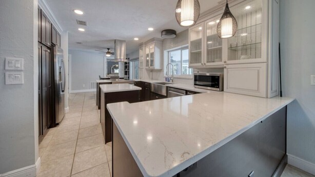 A modern kitchen with white cabinetry, a large island, and pendant lighting. - Lighthouse Retreat With A Pool (Ponce Inlet)