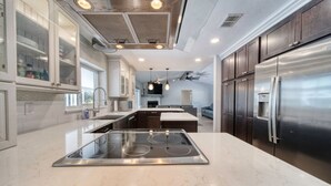 A modern kitchen with a central island, stainless steel appliances, and a dining area in the background. - Lighthouse Retreat With A Pool (Ponce Inlet)