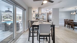 A spacious kitchen with modern appliances, a dining area with a large table, and a view of a swimming pool through large windows. - Lighthouse Retreat With A Pool (Ponce Inlet)