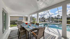 Un'area pranzo esterna moderna con vista sulla piscina, un barbecue e un ampio patio.