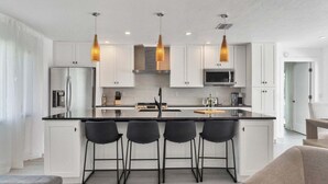 A modern kitchen with white cabinets, a central island with bar stools, stainless steel appliances, and pendant lighting. - Kld1521 (Punta Gorda)