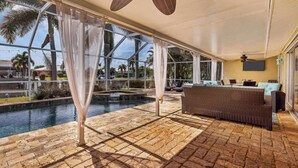 A covered outdoor area with a pool, wicker furniture, and a view of palm trees. - Npl829 (Punta Gorda)