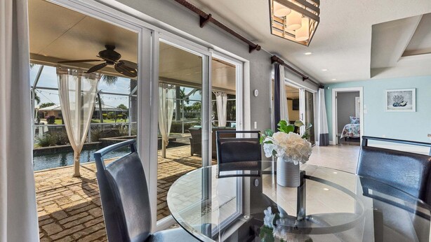 A spacious room with a glass table, chairs, a ceiling fan, and a view of a pool and outdoor area. - Npl829 (Punta Gorda)