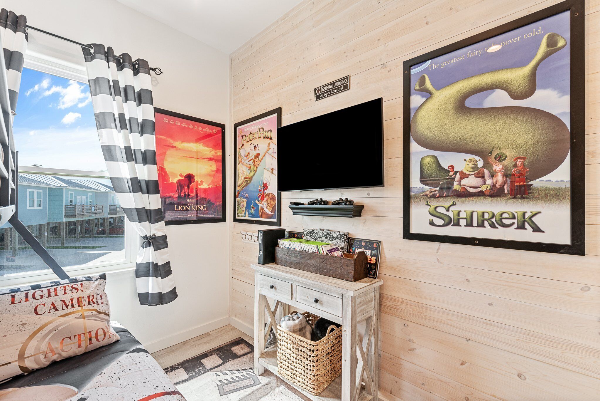 A room with a large window, a flat-screen TV, and posters including 'The Lion King' and 'Shrek'.