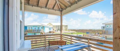 A wooden deck with picnic tables and benches overlooking a beach with buildings in the background.