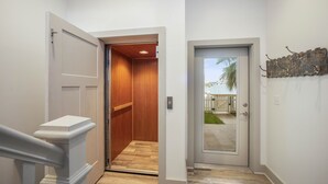 A hallway with a wooden door leading to a room, a white door with a view of the outside, and a decorative metal piece on the wall. - Marina Del Bell - Elevator! Boat Slip for Rent! (Port Aransas)