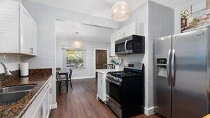 A modern kitchen with a granite countertop, stainless steel appliances, and a dining area with a table and chairs. - Centra Phoenix House Kingbed (Phoenix)