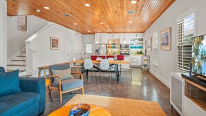 Un interno moderno con soffitto in legno, un'area pranzo con sedie rosse, una cucina con mobili bianchi e un soggiorno con divano blu.
