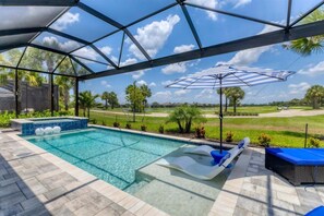 A swimming pool with a view of a golf course, a covered area with a blue umbrella, and a lounge chair. - Heritage Landing Haven Resort Amenities + Golf Membership (Punta Gorda)
