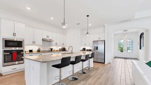 A modern kitchen with white cabinetry, stainless steel appliances, a central island with bar stools, and a large window providing natural light. - Heritage Landing Haven Resort Amenities + Golf Membership (Punta Gorda)