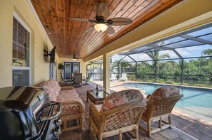 Un patio couvert, aménagé avec des meubles en osier, un barbecue et offrant une vue sur une piscine.
