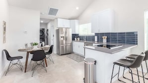 Una cocina moderna con armarios blancos, un refrigerador de acero inoxidable y una pequeña isla con taburetes de bar.