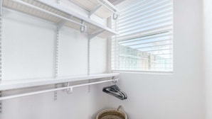 Un cuarto de lavandería con estanterías blancas, un tendedero y una cesta.