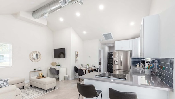 Una cocina moderna con una isla central, electrodomésticos de acero inoxidable y un comedor con una mesa y sillas blancas.