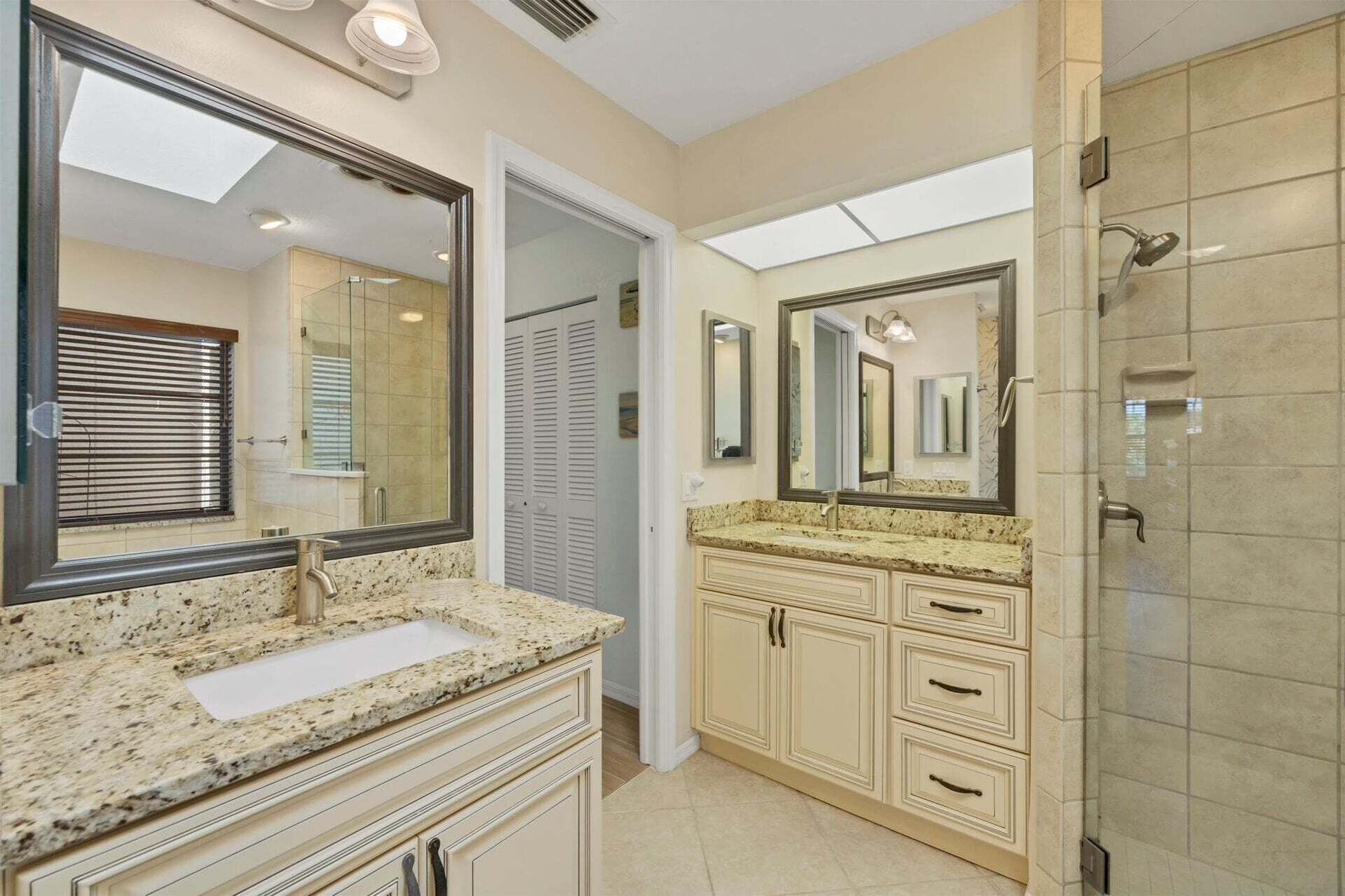 Une salle de bain avec un meuble-lavabo à deux vasques, un grand miroir, une cabine de douche et un puits de lumière.
