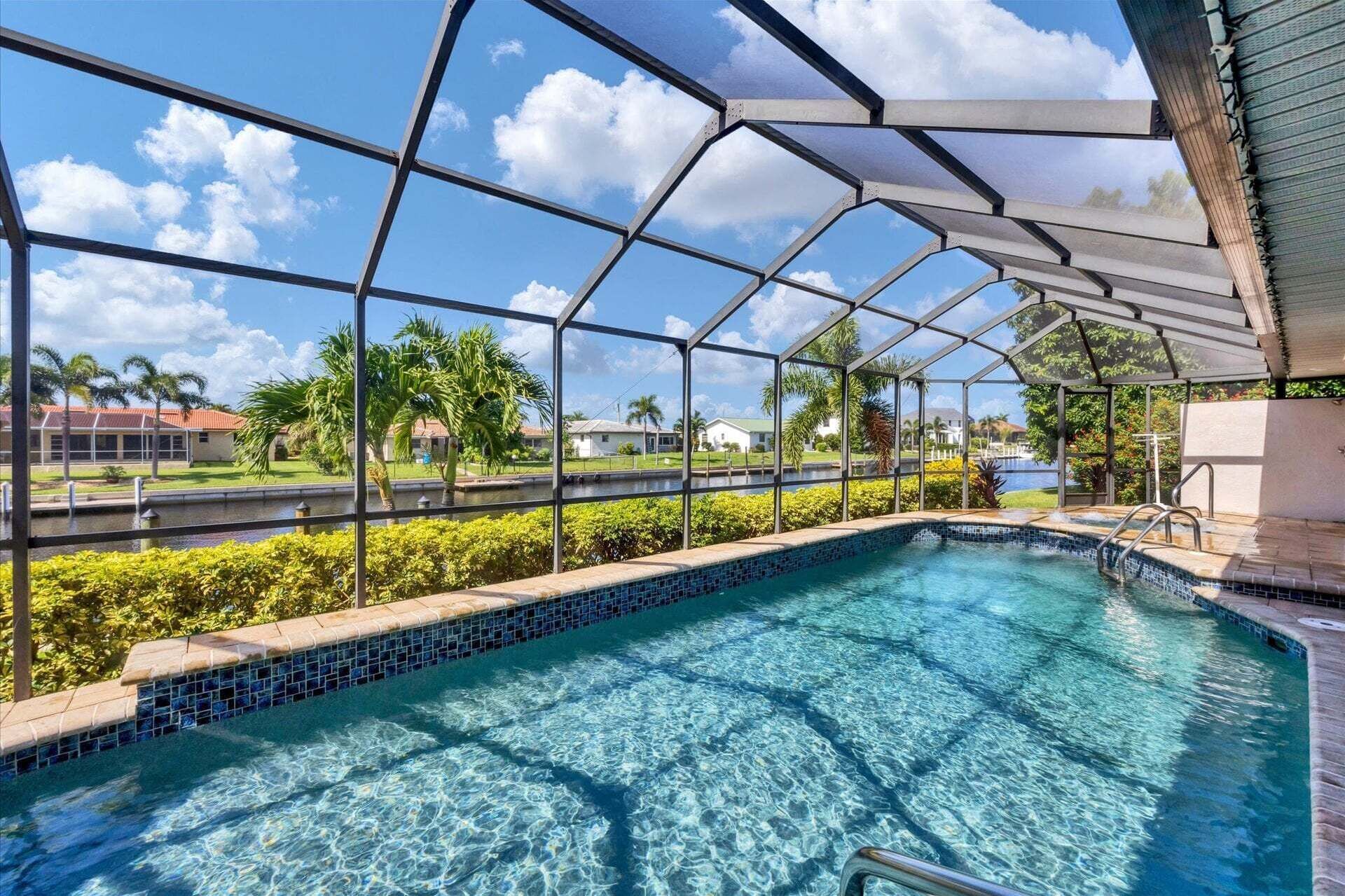A clear swimming pool with a glass enclosure, surrounded by greenery and a view of a residential area.