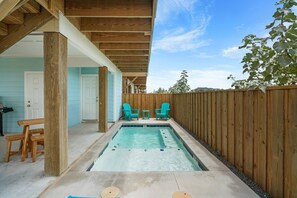 Un patio trasero con piscina, terraza de madera y dos sillas.