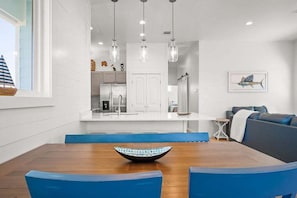 Un comedor moderno con una mesa de madera y sillas azules, una cocina al fondo y un cuadro de un pez en la pared.