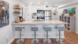 Uma cozinha moderna com armários brancos, bancada de granito, eletrodomésticos de aço inoxidável e três banquetas.