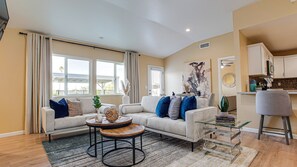 A modern living room with a sofa, coffee table, and a dining area with a chair and a small table. - Heatherbrae Phoenix (Phoenix)