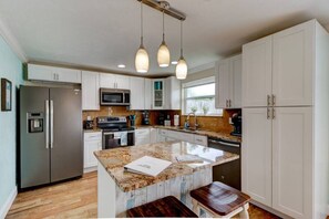 A modern kitchen with white cabinets, stainless steel appliances, a granite countertop, and pendant lighting. - Sunset Oasis by the Boondocks (Port Orange)