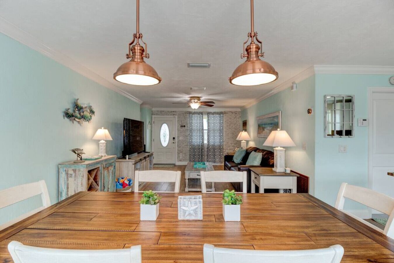 A dining area with a wooden table and chairs, two pendant lights, and a view into the living room.