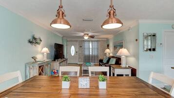 A dining area with a wooden table and chairs, two pendant lights, and a view into the living room.