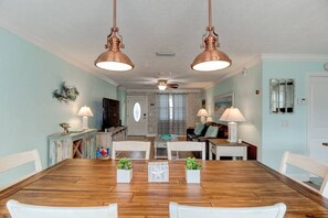 A dining area with a wooden table, white chairs, and two copper pendant lights. - Sunset Oasis by the Boondocks (Port Orange)