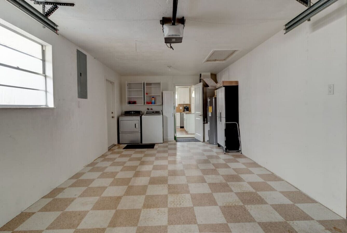 Un pasillo con piso a cuadros, una kitchenette con gabinetes y electrodomésticos, y una puerta que da a otra habitación.