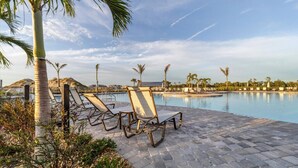 Un área junto a la piscina con sillones de descanso y palmeras.