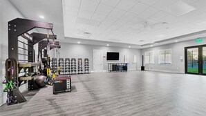 Un gimnasio amplio con diversos equipos de ejercicio, un televisor y una puerta señalizada con 