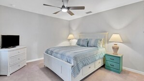 Un dormitorio con una cama, dos mesitas de noche con lámparas, un televisor sobre una cómoda y un ventilador de techo.