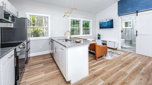 A modern kitchen with a central island, a dining area with a brown chair, and a large window with a view of trees. - H2O Oasis Tree House (Pittsboro)