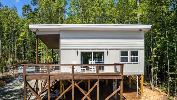 A cabin with a deck, a covered outdoor seating area, and a large window. - H2O Oasis Tree House (Pittsboro)