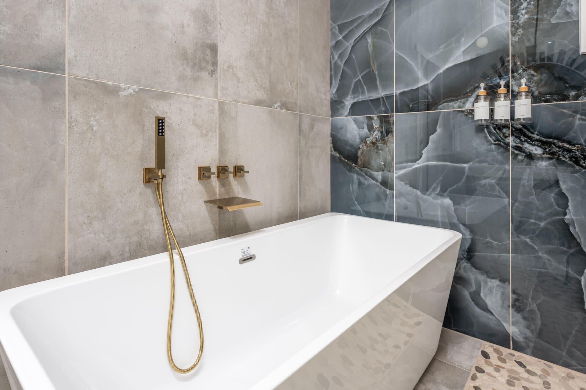 Une salle de bain moderne avec une baignoire blanche, des accessoires dorés et des murs à motifs de marbre.