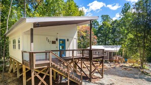 A cabin with a wooden deck and a covered porch, surrounded by trees. - H2O Oasis Tree House (Pittsboro)