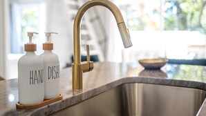 A modern kitchen with a stainless steel sink, a gold faucet, and two white bottles labeled "HAND DISH." - H2O Oasis Tree House (Pittsboro)