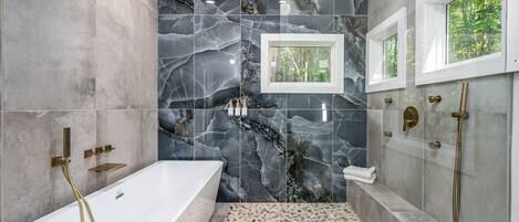 A modern bathroom with a freestanding bathtub, a walk-in shower, and marble walls.