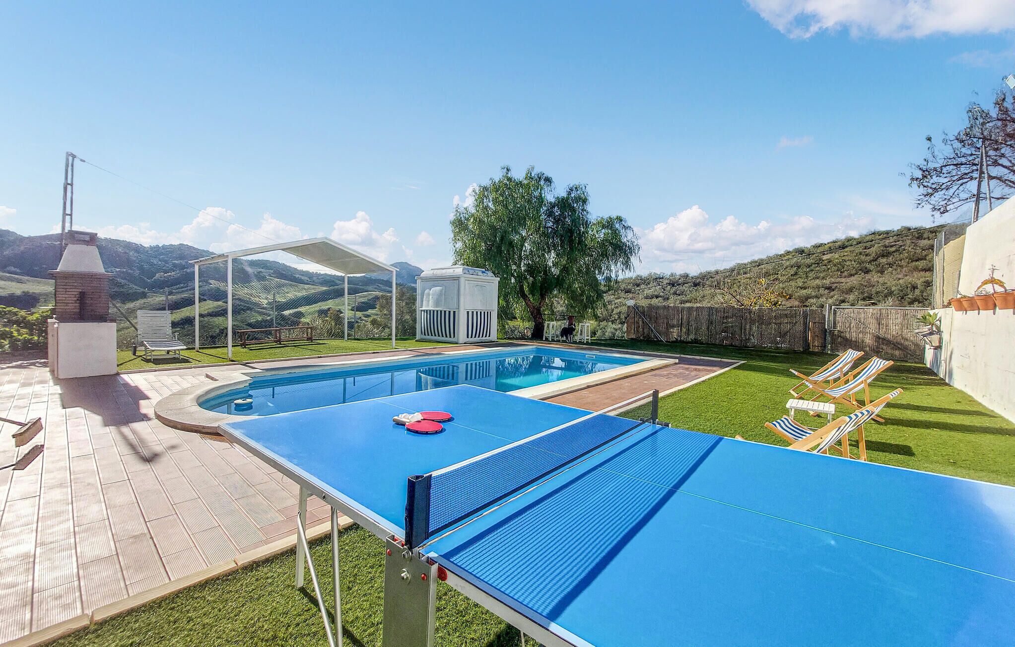 A pool area with a table tennis table, lounge chairs, and a barbecue grill.