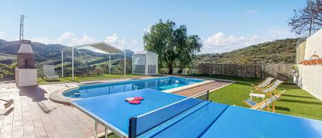A pool area with a table tennis table, lounge chairs, and a barbecue grill.