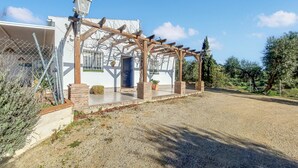 Een huis met een houten pergola, een blauwe deur en een grindpad.