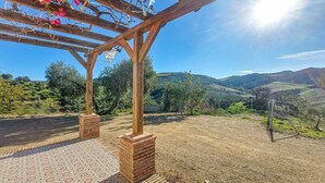 Een houten pergola met een betegelde vloer, bakstenen pilaren en een helder uitzicht op een glooiend landschap.
