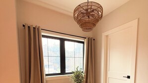 Ein Essbereich mit einem runden Tisch, zwei Stühlen, einer Hängeleuchte, einem Fenster mit Vorhängen und einer Tür.