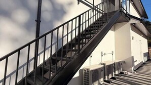 Ein Gebäude mit einer Treppe, die zu einem Balkon führt, Klimaanlagen und einem wolkenlosen Himmel.