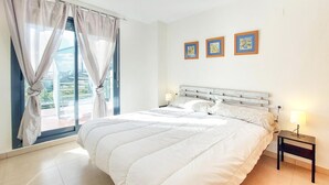 Um quarto com uma cama grande, uma mesinha de cabeceira, uma janela com cortinas e três quadros na parede.