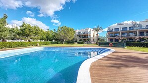 Piscina com deck de madeira, rodeada por vegetação e edifícios modernos.